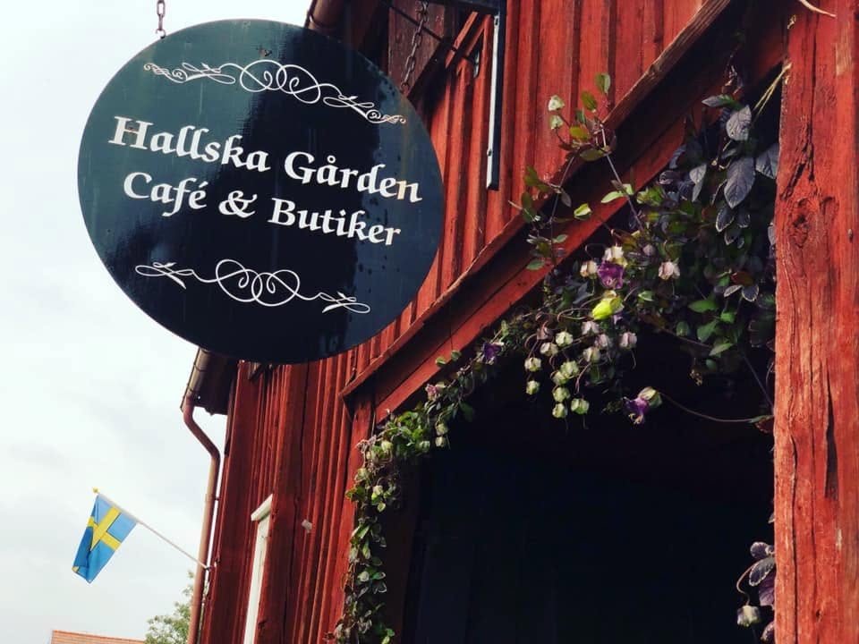 Den runda Hallska Gården Café & Butiker-skylten på den röda träbyggnaden